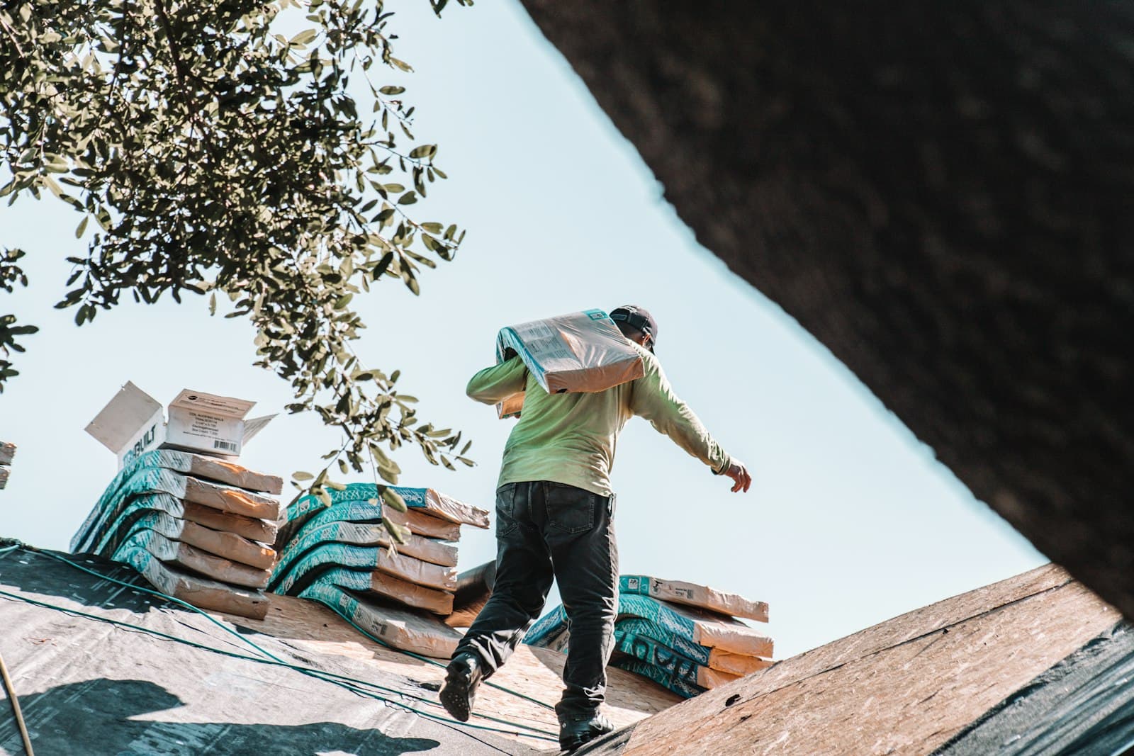 Roofer carrying a bundle of shingles across a roof